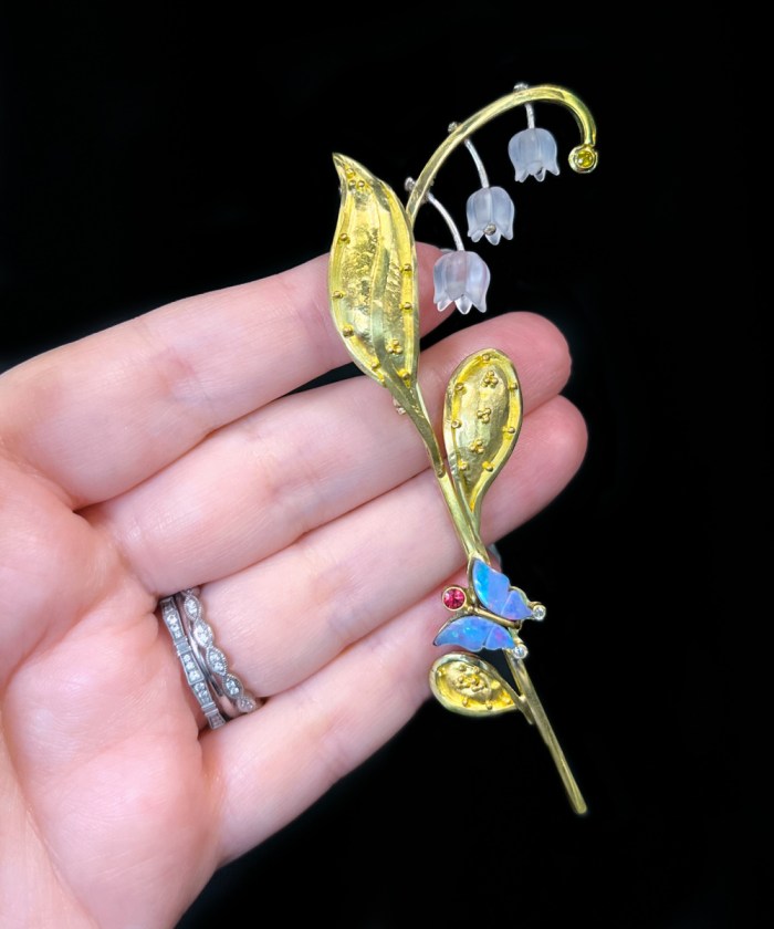 22K and 18K gold and platinum lily and butterfly brooch pendant with Quartz flowers, Opal butterfly. Sheridan Conrad, A Jewelers Art  Seen at AGTA's 2022 Spectrum Awards. 